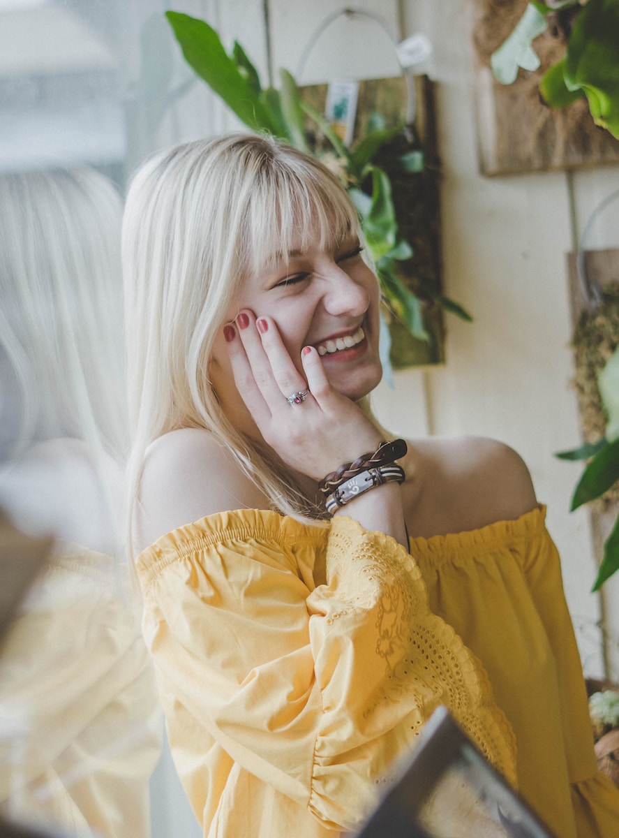 smiling woman in yellow off-shoulder top holding her cheek